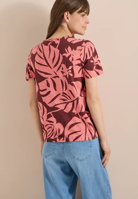Frau von hinten in rosa T-Shirt mit schwarzem Blattmuster und lockeren blauen Jeans.