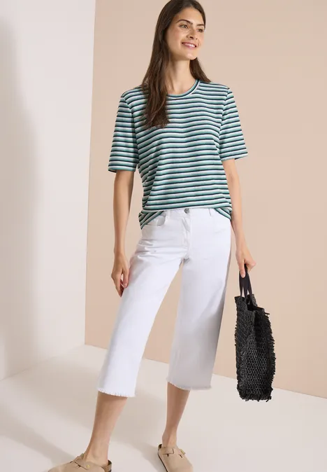 Frau in grünem gestreiftem T-Shirt, weißen Culotte-Hosen und schwarzer Tasche.