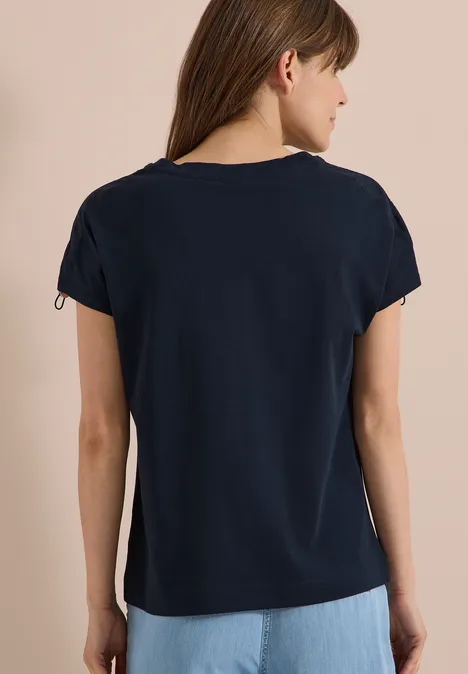 Rückansicht einer Frau in schlichten dunkelblauen T-Shirt vor neutralem Hintergrund.