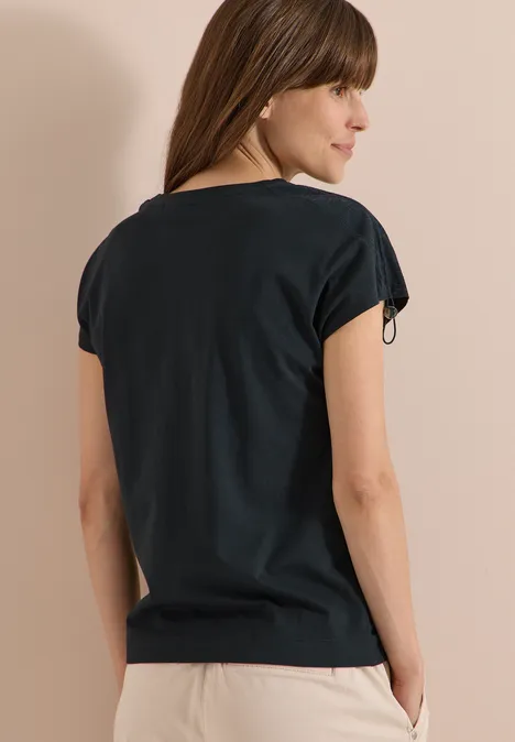 Frau von hinten in schlichtem schwarzem Shirt, Hände lässig in den Taschen