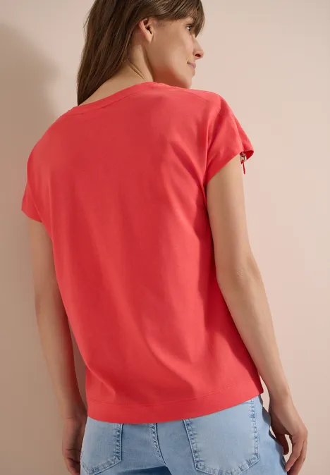 Shirt met rimpels in effen kleur coral Vrouw van achteren in een koraalkleurig t-shirt en lichtblauwe spijkerbroek voor een neutrale achtergrond.