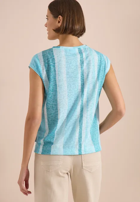 Femme vue de dos portant un chemisier ample à rayures turquoise et blanc, manches courtes.