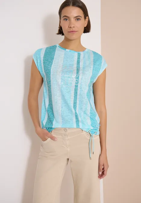 Femme en haut rayé bleu et blanc et pantalon beige sur fond clair.