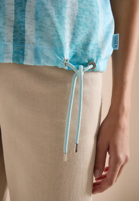 Top turquoise à fines rayures avec cordons de serrage au bas, porté sur pantalon beige.