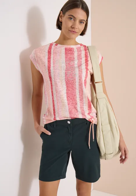 Femme en t-shirt à rayures rose et blanc, short bleu foncé et sac d’épaule.