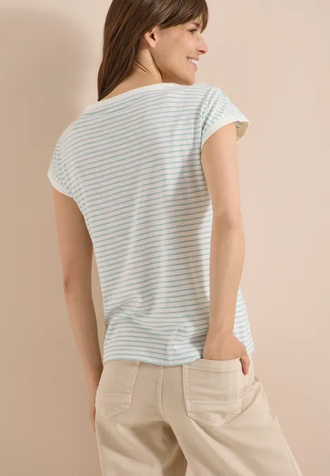 Vrouw van achteren in pastelgestreept t-shirt en beige broek met zakken, lichte achtergrond