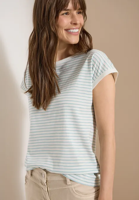 Een vrouw draagt een gestreept T-shirt en beige broek tegen een neutrale achtergrond