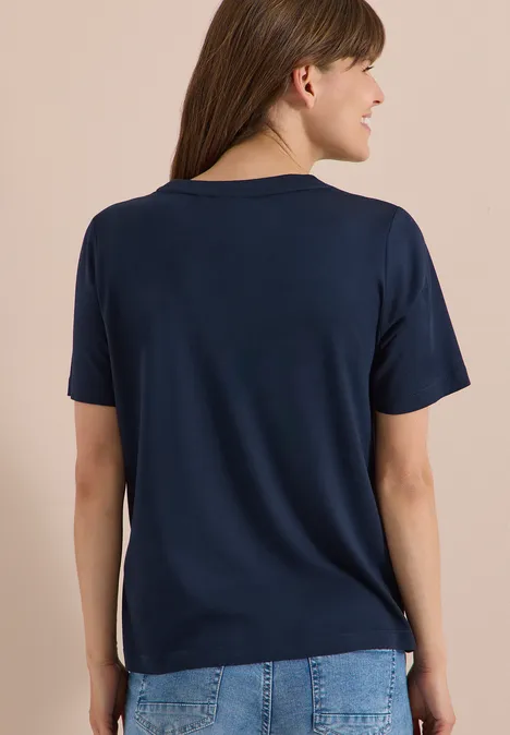Een vrouw gezien van achteren draagt een effen donkerblauw T-shirt en spijkerbroek.