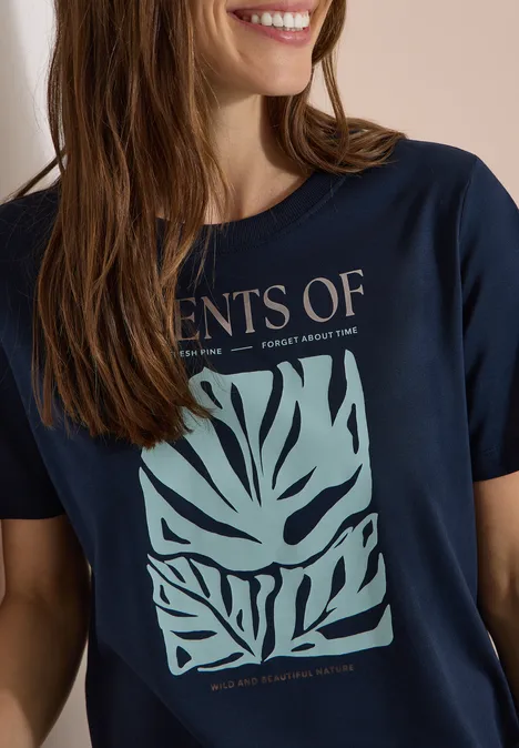 Lachende vrouw in een marineblauw t-shirt met groen abstract bladpatroon.