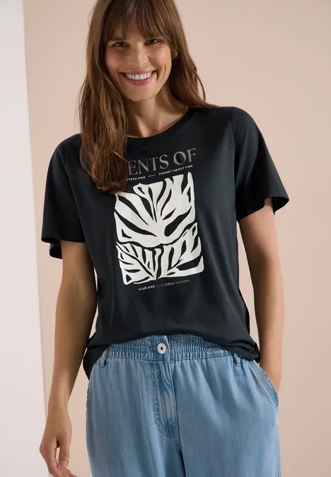 T-Shirt mit Rundhals und Frontprint palm breeze green Frau trägt schwarzes T-Shirt mit weißem Blattmuster und lockere Jeanshose.