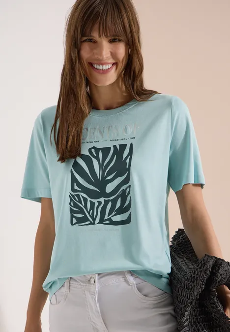 T-Shirt mit Rundhals und Frontprint crystal mint Frau trägt mintgrünes T-Shirt mit schwarzem Blätter-Print, helle Hose, hält schwarze Jacke in der Hand.