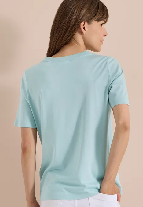 T-Shirt mit Rundhals und Frontprint crystal mint Eine Frau von hinten in locker sitzendem hellblauen T-Shirt vor neutralem Hintergrund.