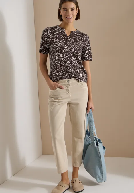 Modisches Outfit: Gemustertes Kurzarmtop, helle, gerade geschnittene Hosen und hellblaue Tasche.