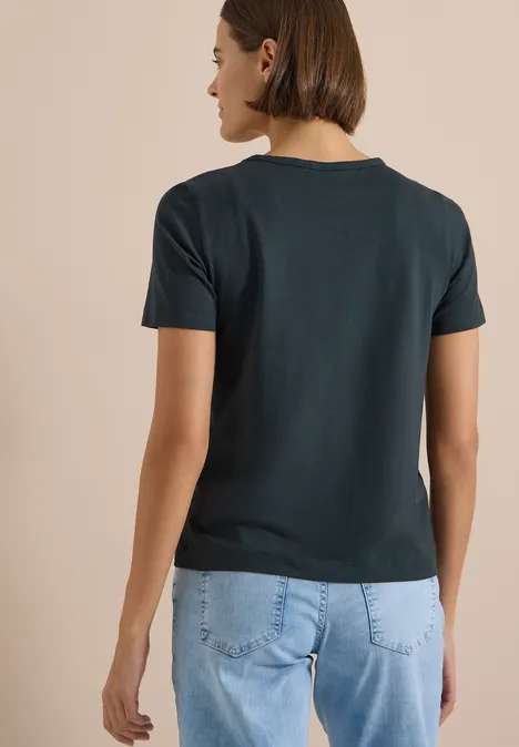 Eine Person von hinten in einem dunkelgrünen T-Shirt und hellblauen Jeans.