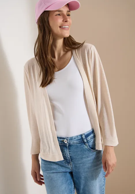 Veste ouverte en couleur unie avec manches 3/4 pearl beige Femme en casquette rose, top blanc, cardigan beige et jean devant un fond neutre.