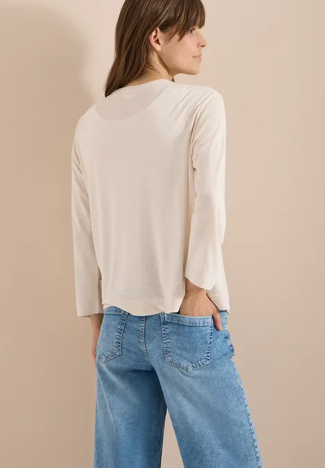 Veste ouverte en couleur unie avec manches 3/4 pearl beige Personne de dos portant un haut à manches longues beige et un jean bleu, une main dans la poche arrière.