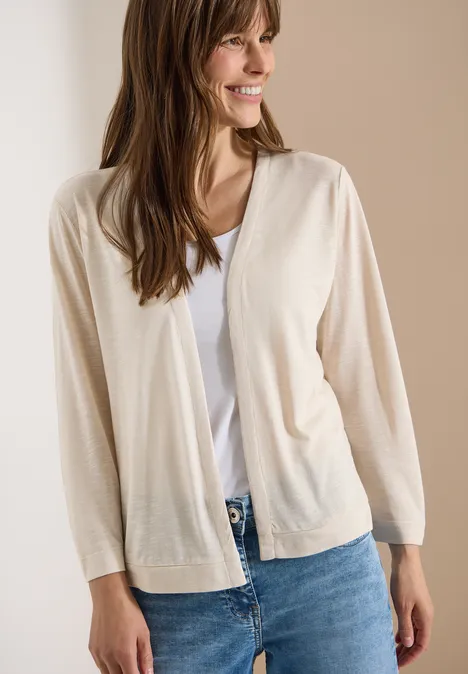 Veste ouverte en couleur unie avec manches 3/4 pearl beige Femme portant un gilet beige, un t-shirt blanc et un jean bleu sur fond épuré.