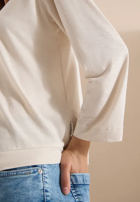 Veste ouverte en couleur unie avec manches 3/4 pearl beige Personne porte un haut crème et un jean bleu, main dans la poche arrière.