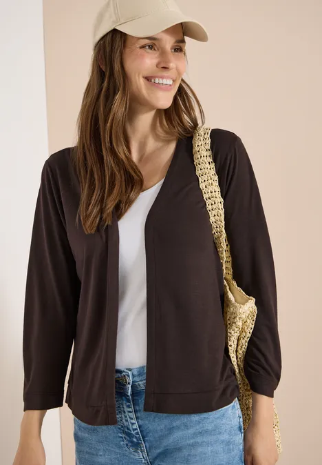 Veste ouverte en couleur unie avec manches 3/4 brown cacao Femme en casquette beige porte un cardigan noir, un top blanc et un sac en raphia.