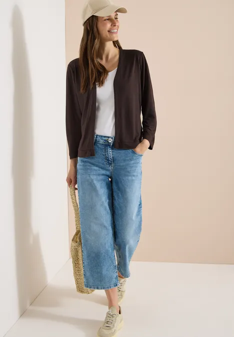 Veste ouverte en couleur unie avec manches 3/4 brown cacao Femme en tenue décontractée: top blanc, veste noire, jean large, baskets, casquette et sac en paille.