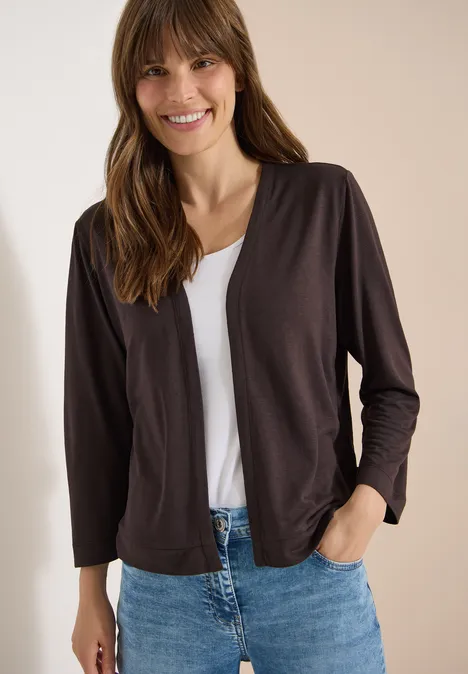 Veste ouverte en couleur unie avec manches 3/4 brown cacao Femme portant un gilet foncé sur un t-shirt blanc et un jean bleu, main dans la poche.