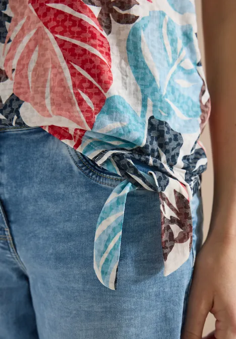 Person trägt blaue Jeans und bunt geblümte Bluse mit seitlichem Knoten.
