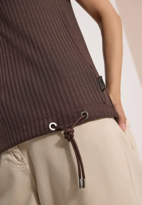 Bruin geribbeld topje met koordsluiting onderaan, gecombineerd met losse, lichtbeige broek.