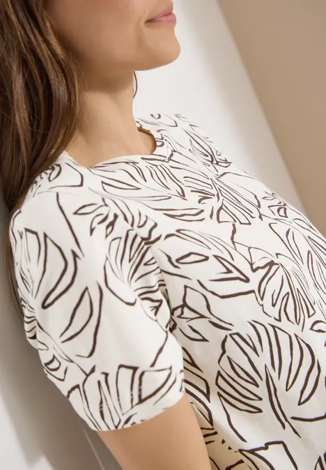 T-Shirt mit Rundhals und Blätterprint light alabaster white Ein Ausschnitt einer Frau in einem weißen T-Shirt mit schwarzem Blattmuster.