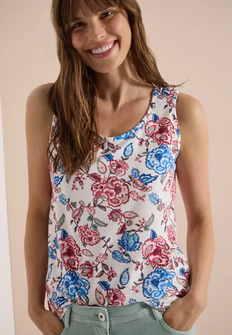 Frau in ärmellosem Top mit blau-rotem Blumenprint vor neutralem Hintergrund.