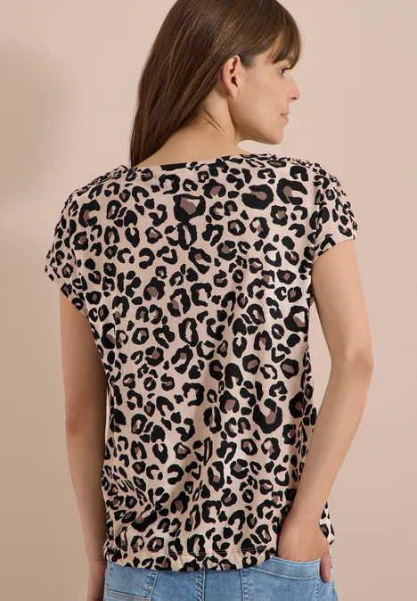 Frau von hinten in beige-schwarzem Leopardenmuster-T-Shirt vor hellem Hintergrund.