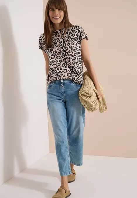 Frau trägt Leoparden-T-Shirt, blaue Jeans und Strohtasche.