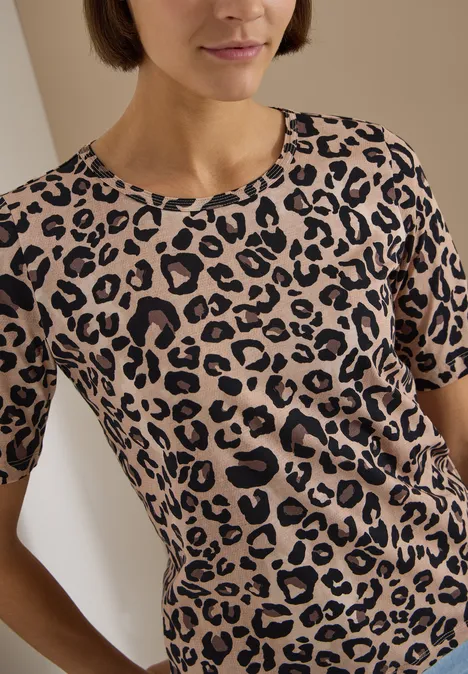 Frau mit kurzem braunem Haar trägt beiges T-Shirt mit schwarzem Leopardenmuster.