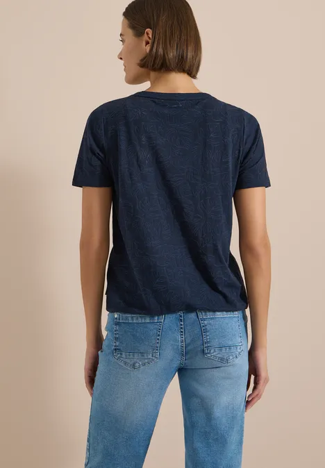 Shirt met burn-out look universal blue Een persoon van achteren draagt een donkerblauw T-shirt en een blauwe spijkerbroek voor een beige achtergrond.