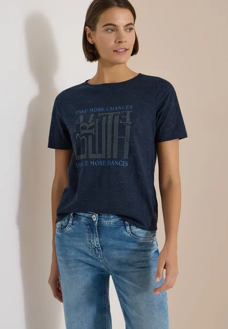 Shirt met burn-out look universal blue Vrouw in neutrale omgeving draagt donkerblauw T-shirt met print en blauwe spijkerbroek.