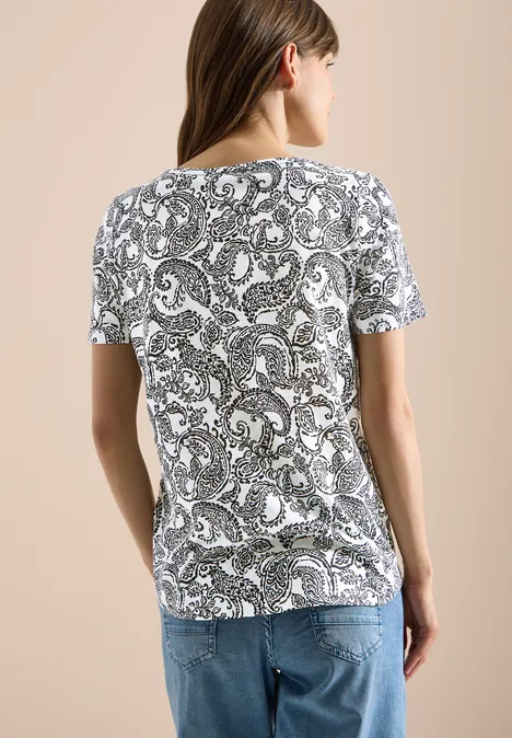 T-Shirt mit Rundhals und Muster Black Frau in weißem T-Shirt mit schwarzem Paisley-Muster und blauer Jeans, Rückansicht.
