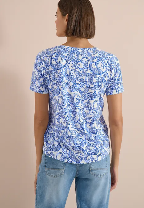 T-Shirt mit Rundhals und Muster vanilla white Rückansicht einer Frau in kurzem, blau-weiß gemustertem T-Shirt und hellblauen Jeans vor beigem Hintergrund.