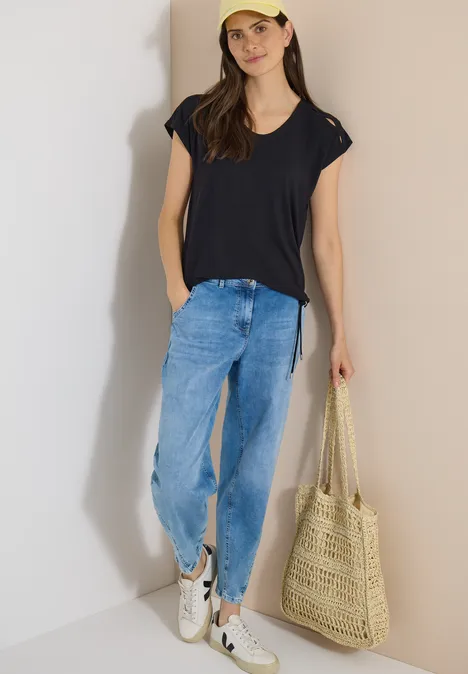 T-shirt à épaules tombantes avec découpe Black Femme en tenue décontractée : T-shirt bleu foncé, jean ample, baskets blanches et sac en paille.