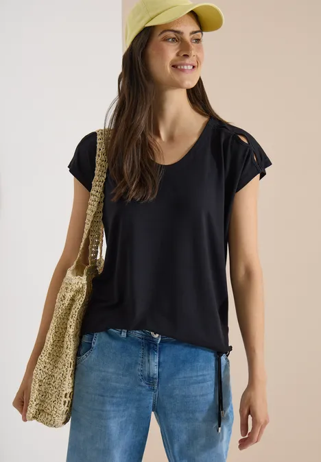 T-shirt à épaules tombantes avec découpe Black Personne en T-shirt noir, jean, casquette jaune et sac en paille, posant devant un fond neutre.