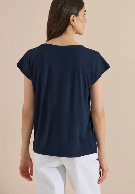 T-shirt à épaules tombantes avec découpe universal blue Une femme vue de dos porte un t-shirt bleu marine à manches courtes et un pantalon blanc sur fond neutre.
