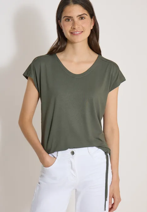 Shirt met afhangende schouders en uitgesneden detail khaki Vrouw in olijfgroene T-shirt met korte mouwen en witte broek.