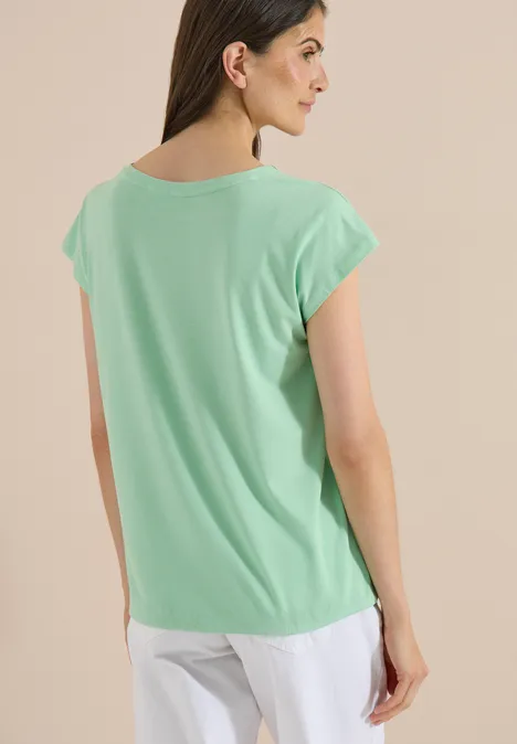 T-shirt à épaules tombantes avec découpe juicy lime Femme de dos portant un t-shirt vert menthe et un pantalon blanc sur fond neutre.