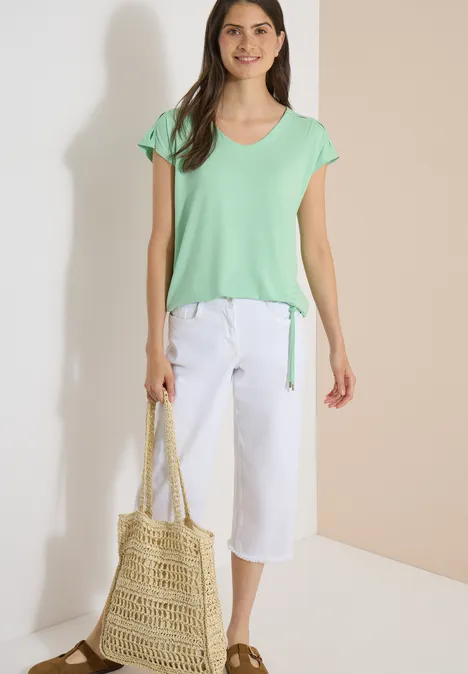 T-shirt à épaules tombantes avec découpe juicy lime Femme en t-shirt vert menthe et pantalon blanc court, tenant un sac en paille.