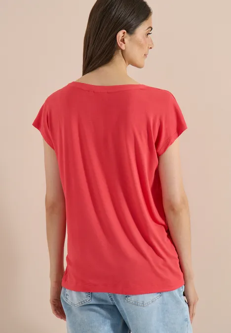 T-shirt à épaules tombantes avec découpe coral Femme de dos portant un t-shirt rouge à manches courtes et un jean bleu sur fond neutre.