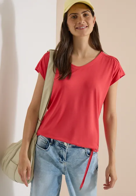 T-shirt à épaules tombantes avec découpe coral Femme portant un t-shirt rouge, un jean et un sac en bandoulière sur fond clair.