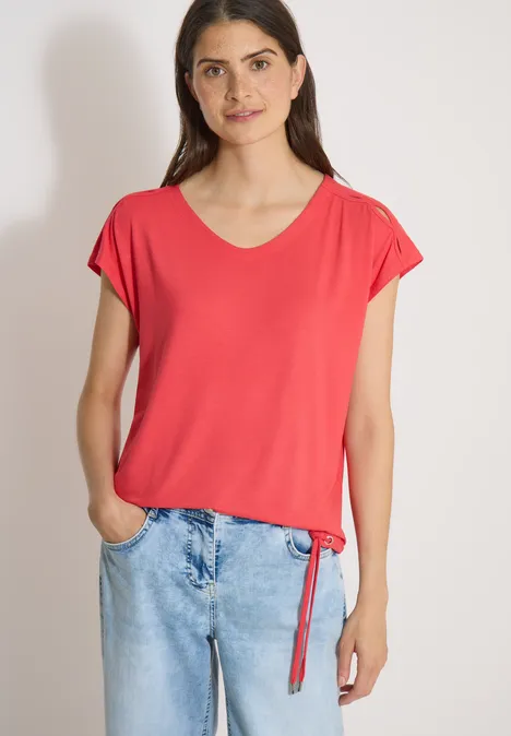 T-shirt à épaules tombantes avec découpe coral Femme décontractée portant un t-shirt rouge et un jean, mains dans les poches.