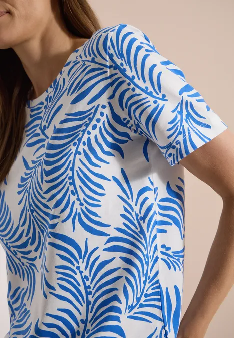 Weißes T-Shirt mit blauem Blattmuster, am Modell vor neutralem Hintergrund.