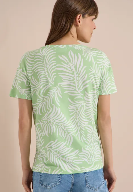 Rückenansicht einer Frau in grünem T-Shirt mit weißem Blattmuster und blauen Jeans.