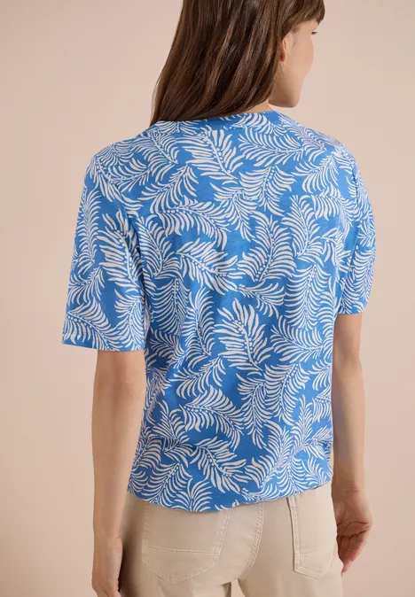 Shirt met gespleten hals en print ethereal blue Vrouw van achteren in een blauw T-shirt met wit bladpatroon en een beige broek.