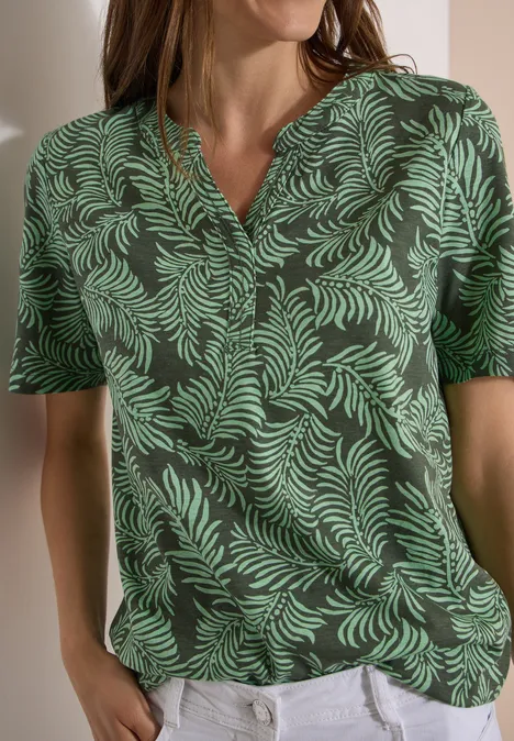 Shirt met gespleten hals en print khaki Vrouw in groen V-shirt met bladpatroon en witte broek.