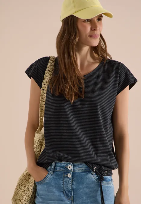 Vrouw in gestreept donkerblauw T-shirt, spijkerbroek, strohoed en gevlochten schoudertas.